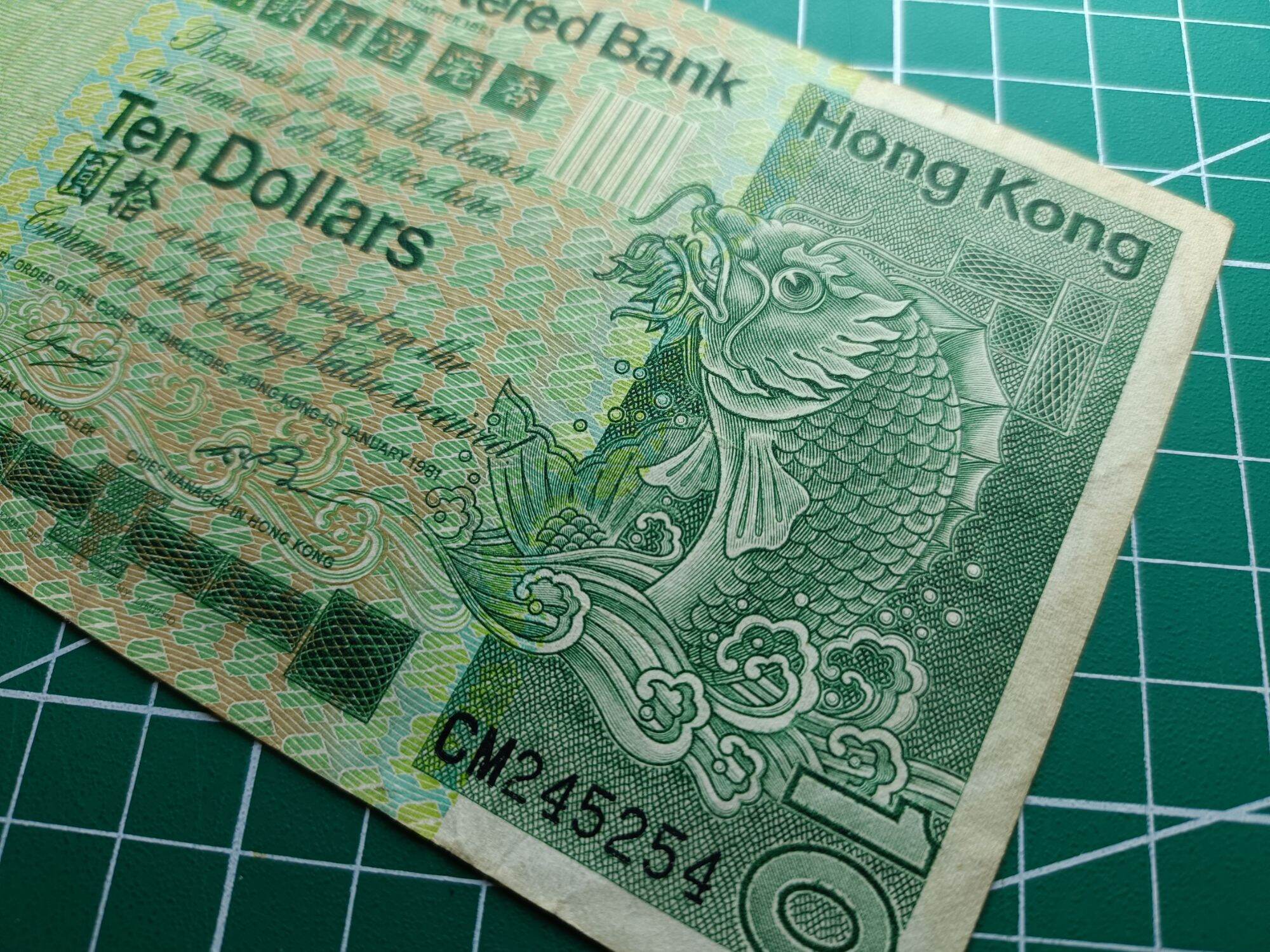 Hong Kong 10 Dollars ( 10 HKD) 1980 - 1981. Issues by Standard Chartered Bank ( Hong Kong). Green Multicolored underprint With Large Carp On The Right Hand Side.  Watermark. Helmeted Warrior's Head  Condition GVF. Nice Prefix : CM 245254. 