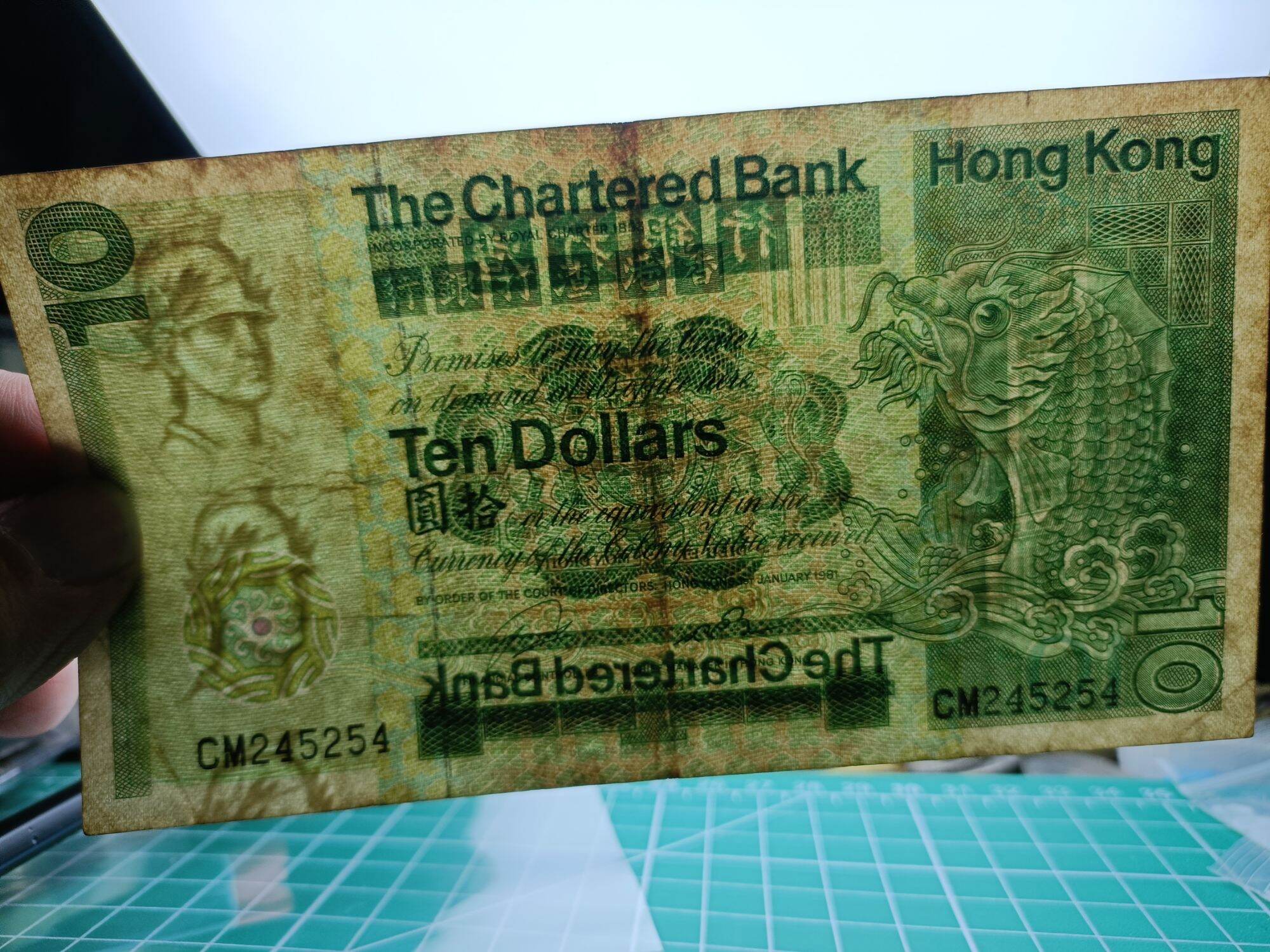 Hong Kong 10 Dollars ( 10 HKD) 1980 - 1981. Issues by Standard Chartered Bank ( Hong Kong). Green Multicolored underprint With Large Carp On The Right Hand Side.  Watermark. Helmeted Warrior's Head  Condition GVF. Nice Prefix : CM 245254. 