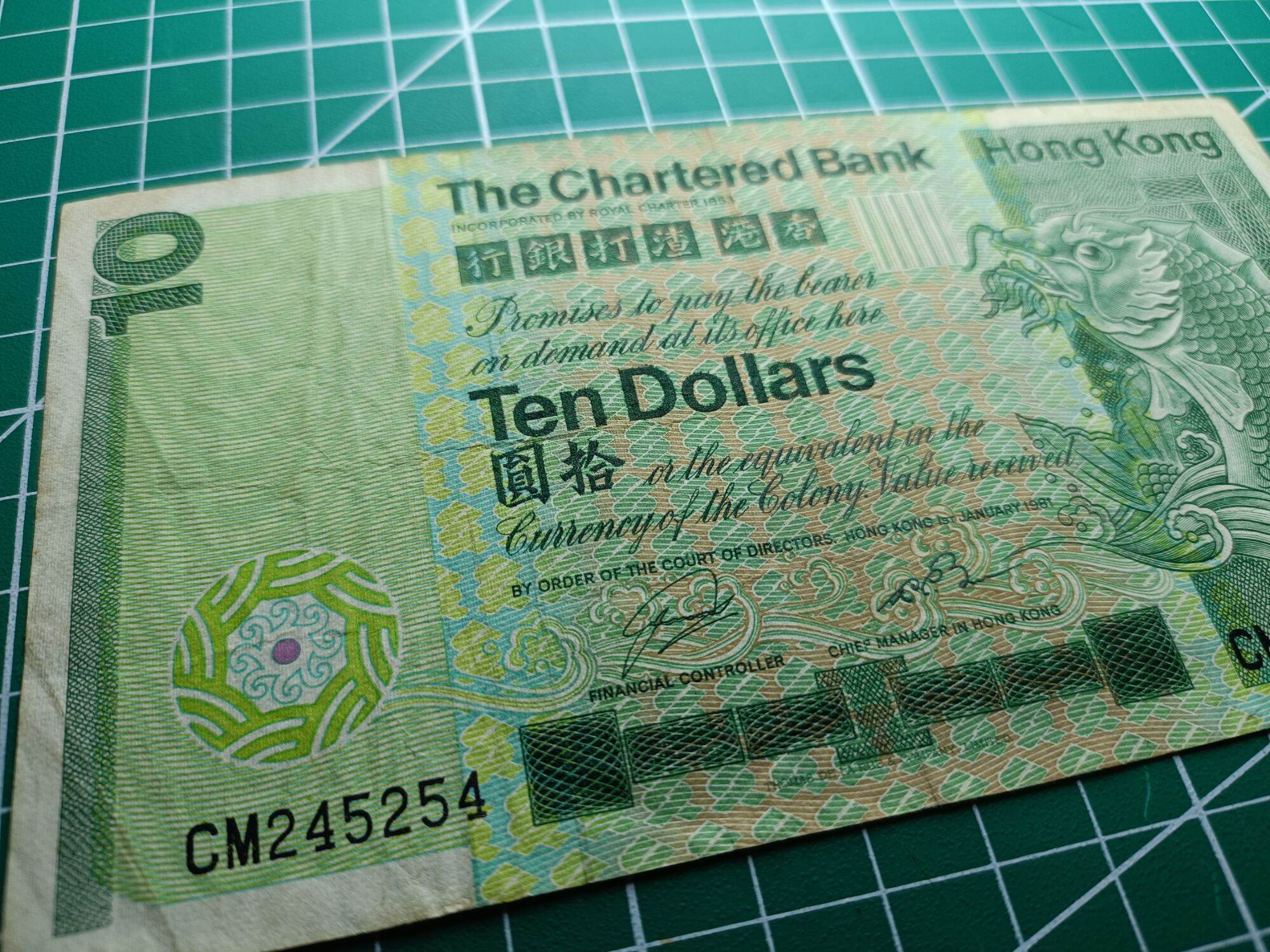 Hong Kong 10 Dollars ( 10 HKD) 1980 - 1981. Issues by Standard Chartered Bank ( Hong Kong). Green Multicolored underprint With Large Carp On The Right Hand Side.  Watermark. Helmeted Warrior's Head  Condition GVF. Nice Prefix : CM 245254. 