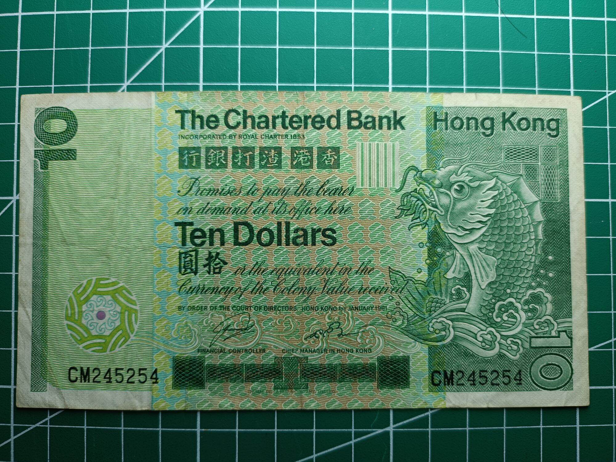 Hong Kong 10 Dollars ( 10 HKD) 1980 - 1981. Issues by Standard Chartered Bank ( Hong Kong). Green Multicolored underprint With Large Carp On The Right Hand Side.  Watermark. Helmeted Warrior's Head  Condition GVF. Nice Prefix : CM 245254